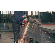 Un bărbat taie o bucată de metal cu un polizor unghiular.