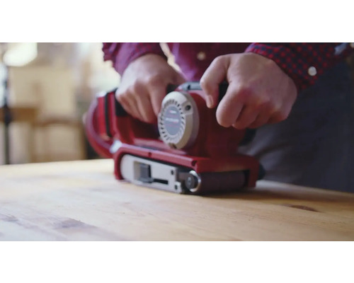 O persoană folosește o șlefuitoare cu bandă pe o suprafață de lemn.