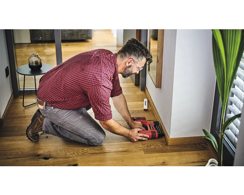 Un bărbat fixează plintele de perete cu un capsator electric