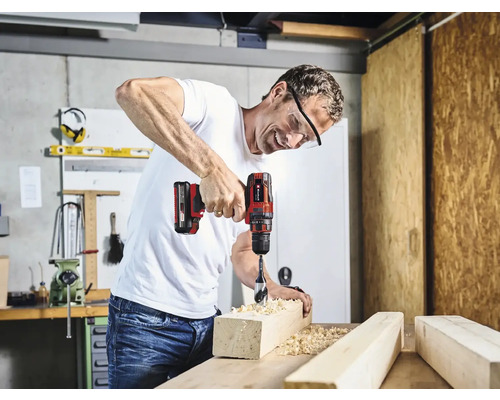 Un bărbat găurește o bucată de lemn cu o șurubelniță electrică într-un atelier.