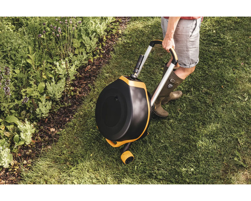 Scenă de grădină cu un compostor rotativ pe roți, ținut de o persoană pe un gazon