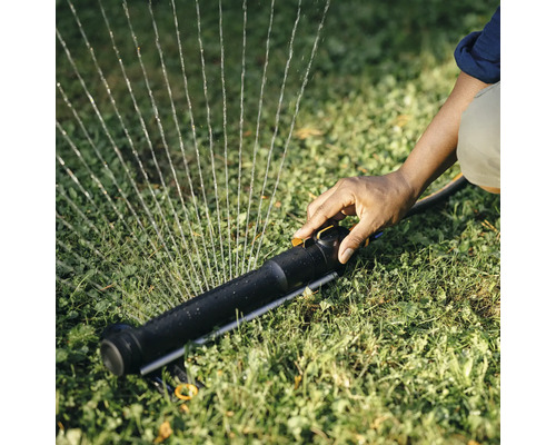 O persoană operează un aspersor de gazon pe un gazon.