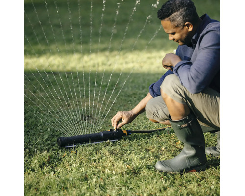O persoană ajustează un aspersor de gazon în grădină.