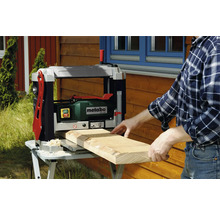 Un bărbat rindeluiește o scândură de lemn cu o mașină de rindeluit Metabo