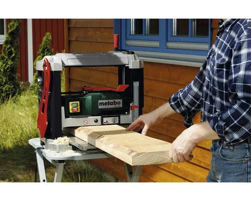 Un bărbat rindeluiește o scândură de lemn cu o mașină de rindeluit Metabo