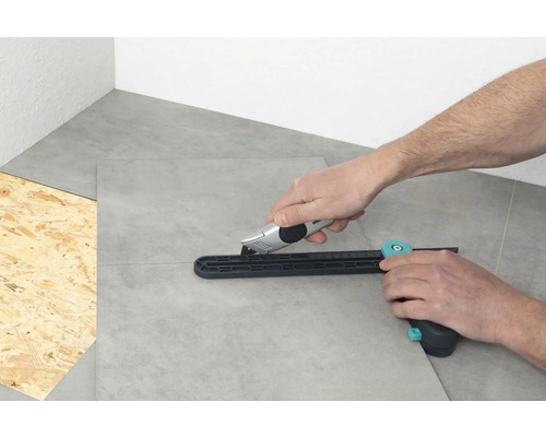 Persoană care taie plăci ceramice cu un tăietor de plăci și un cuțit de tăiat