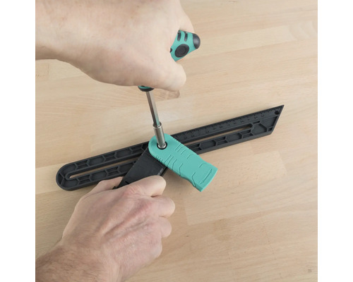 O persoană ajustează un șablon de unghi cu o șurubelniță pe o podea de lemn.