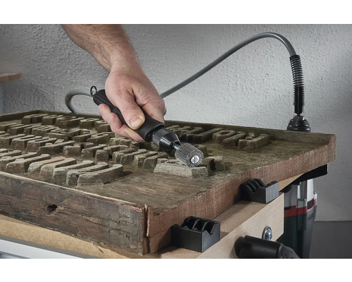 O persoană folosește un instrument multifuncțional cu ax pe o suprafață de lemn pentru a o prelucra.