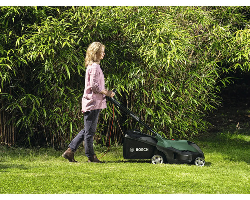 Femeie folosind o mașină de tuns iarba în grădină