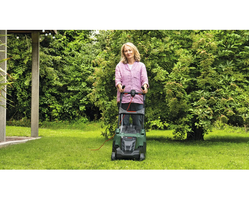 Femeie folosind o mașină de tuns iarba în grădină.