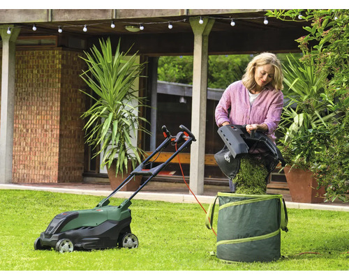 Femeie care varsă iarba dintr-o mașină de tuns iarba într-un sac de grădină în grădină.