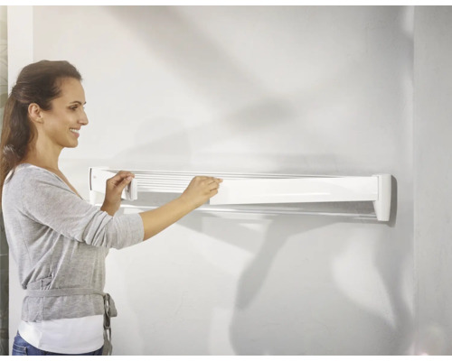 Femeie care manevrează un uscător de rufe alb, montat pe perete.