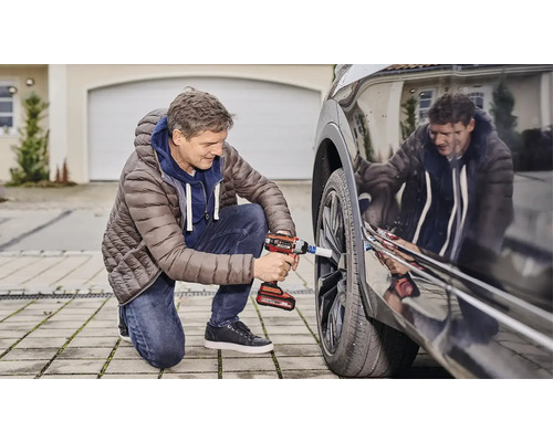 Un bărbat schimbă o roată de mașină cu o cheie de impact cu acumulator