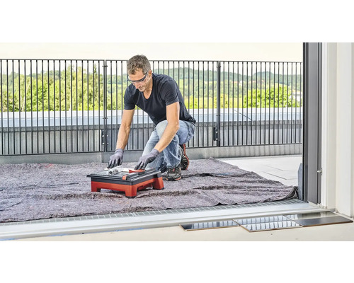 Un bărbat taie plăci ceramice cu o mașină de tăiat plăci pe un balcon.