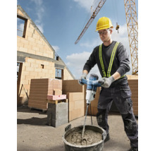 Un muncitor în construcții amestecă mortar cu un mixer electric pe un șantier.