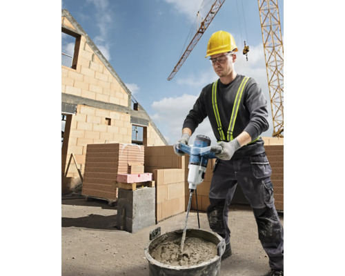 Un muncitor în construcții amestecă mortar cu un mixer electric pe un șantier.