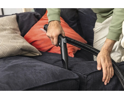 Persoană curățând canapeaua cu duza aspiratorului