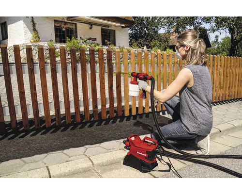 Femeie pulverizează gard din lemn cu sistem de pulverizare vopsea de la Einhell