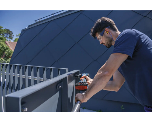 Un bărbat montează o balustradă metalică cu o șurubelniță electrică, purtând ochelari de protecție și căști antifoane.