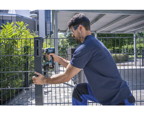 Un bărbat montează un stâlp de gard cu o șurubelniță electrică.