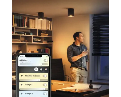 Scenă de birou cu o persoană care se uită pe fereastră și un smartphone cu o aplicație pentru controlul luminilor