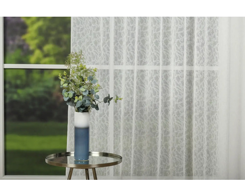 Fereastră decorativă cu perdea transparentă, masă și vază de flori.