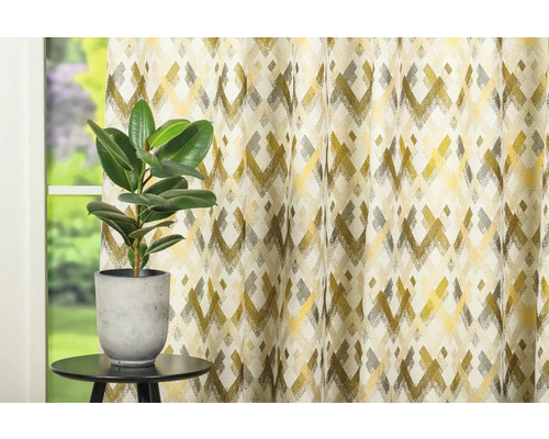 Cortină decorativă cu model geometric lângă o plantă de interior pe o masă.