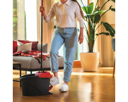 Femeie care folosește mop și găleată pentru a curăța camera de zi.