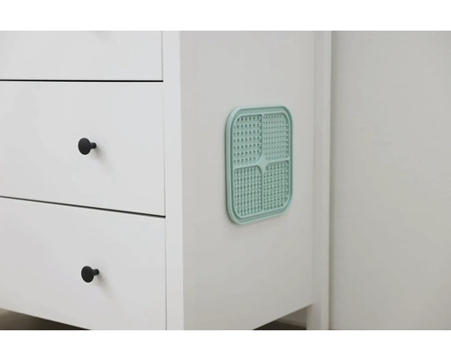 Prim-plan cu un dulap de baie alb cu o grilă de aerisire turcoaz.