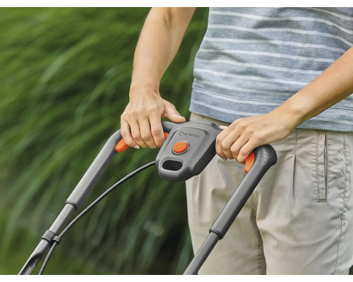 Persoană care operează o mașină de tuns iarba în grădină.