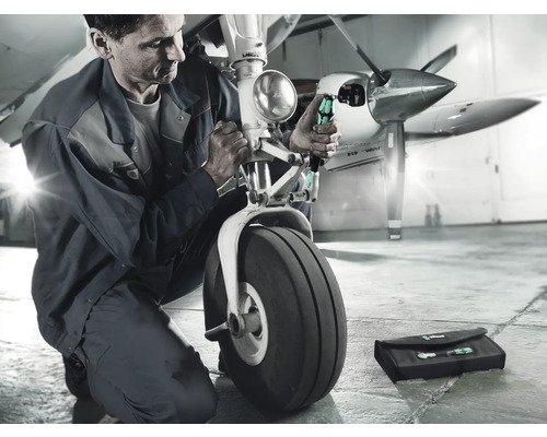 Un mecanic repară trenul de aterizare al unui avion cu șurubelnițe și o trusă de scule.