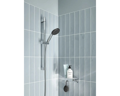 Bară de duș cu duș de mână și raft într-un duș placat cu gresie deschisă.