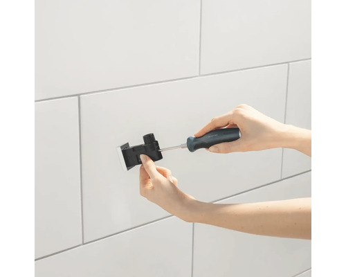 Instalarea unui rezervor de spălare cu o șurubelniță pe un perete placat cu faianță.