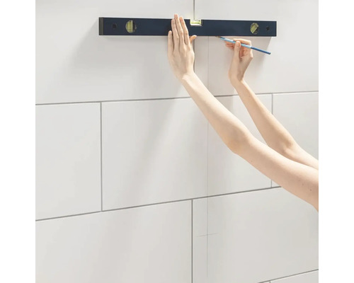 O persoană folosește un nivel cu bulă și un creion pentru a trage o linie pe plăci.