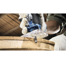 O freză verticală în acțiune în timpul prelucrării unei bucăți de lemn. Operatorul poartă mănuși de lucru.