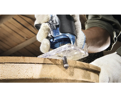 O freză verticală în acțiune în timpul prelucrării unei bucăți de lemn. Operatorul poartă mănuși de lucru.