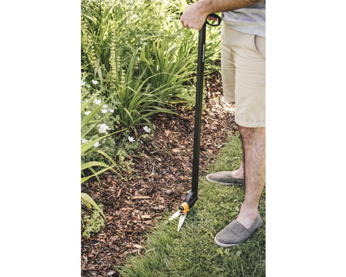 Persoană taie marginea gazonului cu o foarfecă de gazon cu mâner în grădină.