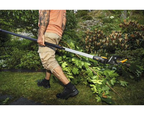 O persoană taie ramuri într-o grădină cu un foarfece telescopic de crengi.