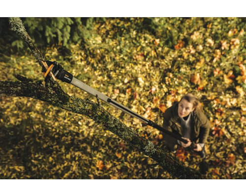 Femeie care folosește un foarfece de crengi cu mâner telescopic pentru a tăia un copac.