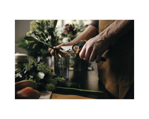 O persoană taie crengi cu o foarfecă de grădină Fiskars pe o masă.