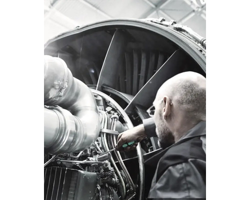 Un bărbat repară un motor de avion cu o șurubelniță.