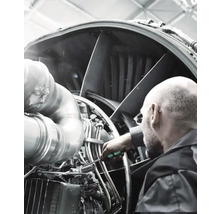 Un bărbat inspectează un motor de avion cu o șurubelniță.