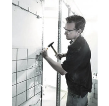 Bărbat cu ochelari de protecție îndepărtează plăcile cu ciocanul și dalta.