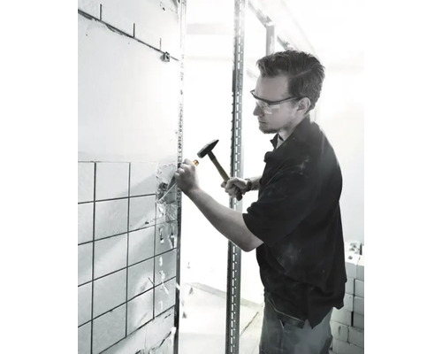 Bărbat îndepărtând plăci ceramice cu ciocanul și dălta în timpul renovării