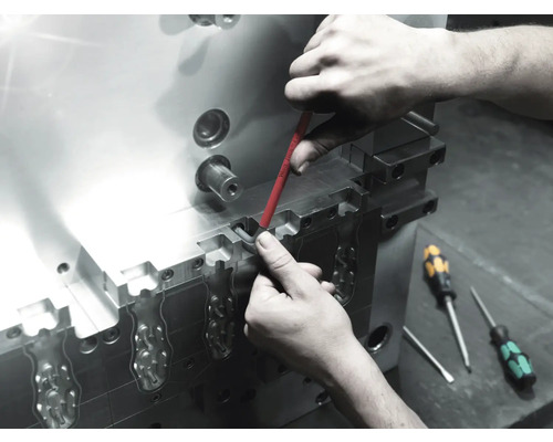 Un muncitor efectuează întreținerea unei scule metalice cu o șurubelniță.