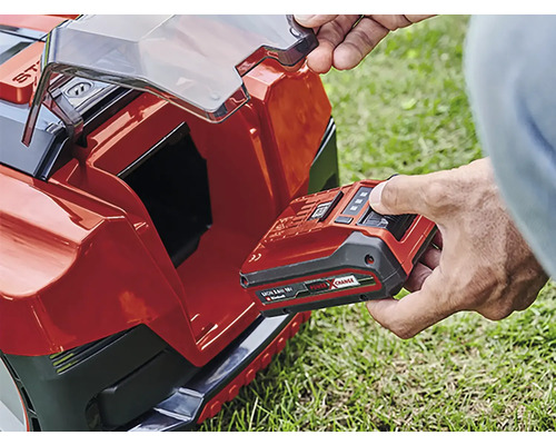 Un bărbat introduce bateria în robotul de tuns iarba.