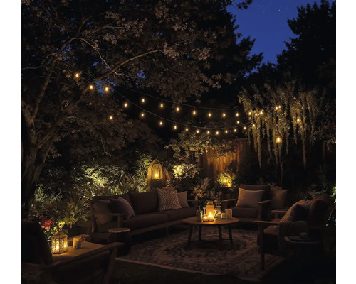 O zonă de grădină cu canapea, scaune, masă și ghirlande luminoase pe timp de noapte.