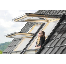 Femeie care se uită pe fereastra de mansardă deschisă cu țigle gri