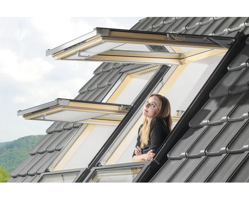 Femeie care se uită pe fereastra de mansardă deschisă cu țigle gri
