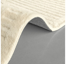 Detaliu al unui covor de culoare deschisă, cu o textură țesută și un colț ondulat care arată partea inferioară